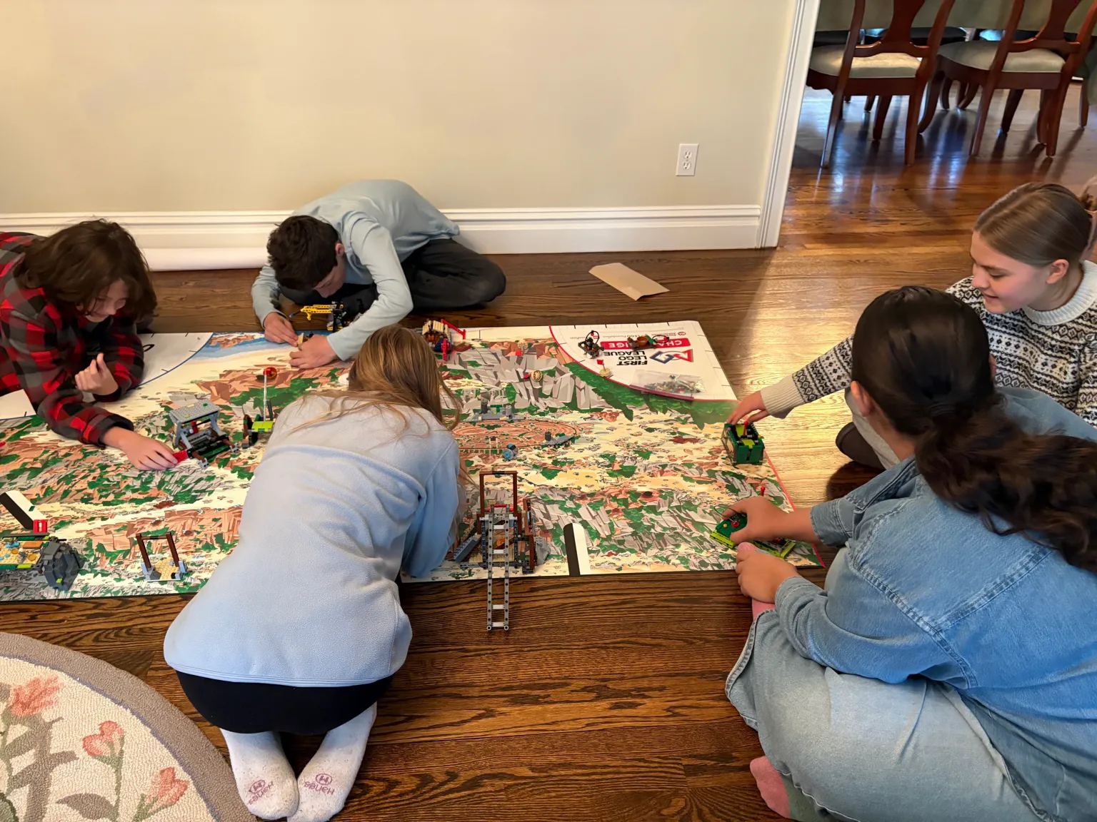 Students kneeling on the floor while adjusting different FLL mission models